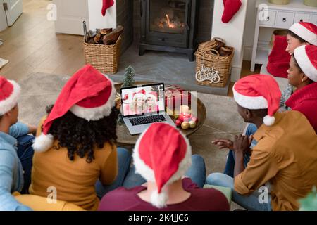 Amici biraciali a babbo natale cappelli sul laptop videochiamata di natale con sorridente madre e figlia. natale, festa e tecnologia di comunicazione. Foto Stock