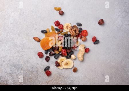 Vista dall'alto di frutta secca, frutti di bosco e noci come ingrediente per un pasto gustoso e sano su sfondo grigio cemento Foto Stock