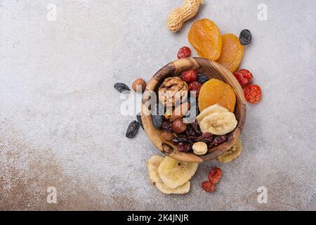 Vista dall'alto della ciotola di legno con frutta secca, frutti di bosco e noci come ingrediente per un pasto gustoso e sano su fondo grigio cemento Foto Stock