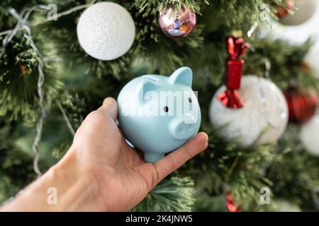 Sotto l'albero di Natale sono scatole con i regali. Sulla scatola c'è una piccola banca di porcellini. Bella carta festiva. Foto Stock