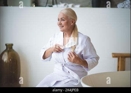 Donna allegra e attraente che pettina il suo ponytail con un pennello per capelli Foto Stock