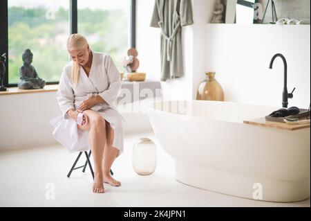 Donna matura allegra che si asciuga la pelle prima di bagnarsi Foto Stock