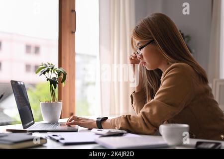 Vista laterale di una giovane donna d'affari che analizza statistiche o dati commerciali su un computer portatile Foto Stock