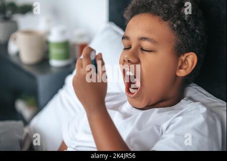 Ragazzo malato che ha mal di gola e spruzzando il rimedio Foto Stock