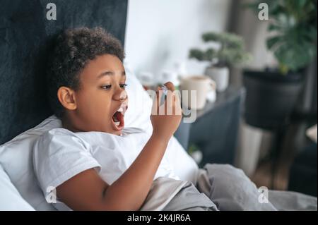 Ragazzo malato che ha mal di gola e spruzzando il rimedio Foto Stock