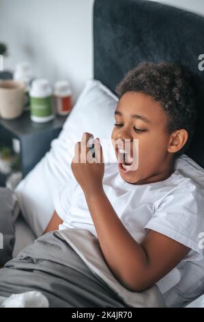 Ragazzo malato che ha mal di gola e spruzzando il rimedio Foto Stock