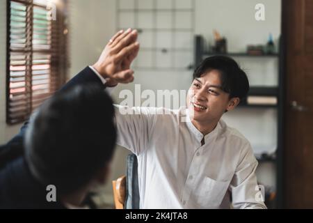 I colleghi maschi sorridenti celebrano il successo condiviso. Lavorare insieme con il sorriso sul viso dando alti cinque in ufficio Foto Stock