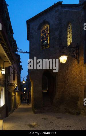 Strada tipica di notte con lampada di fronte a una cappella a le Mont Saint Michel, Normandia, Francia Foto Stock