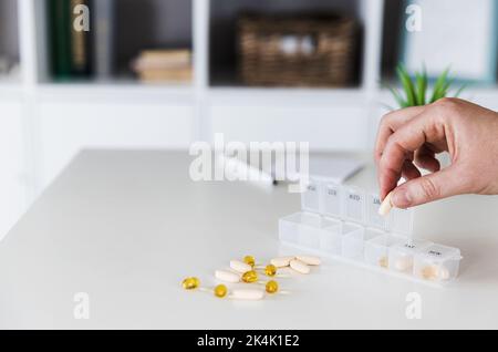 Primo piano delle mani anziane femminili che ordinano, organizzano le pillole. Scatola per pillola medica con dosi di compresse per l'assunzione quotidiana con farmaci bianchi, gialli, beige, capsule. Giovane donna ottenere le sue vitamine quotidiane a casa Foto Stock