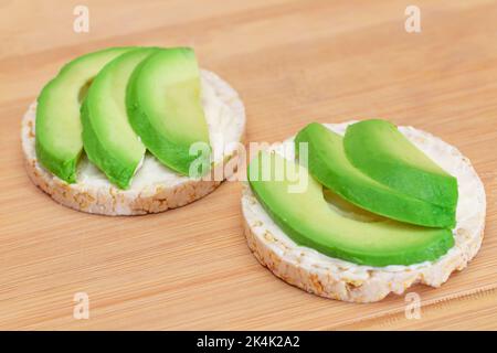 Sandwich con torta di riso con avocado fresco e formaggio cremoso sul tagliere di bambù. Colazione facile. Dieta alimentare. Panini veloci e sani. Croccante con gustoso ripieno. Snack dietetico sano Foto Stock