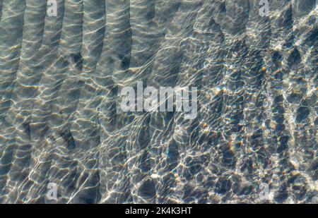 Fondale sabbioso o pavimento marino visto attraverso acqua di mare limpida con luce solare riflessa sulla superficie del mare. Foto Stock
