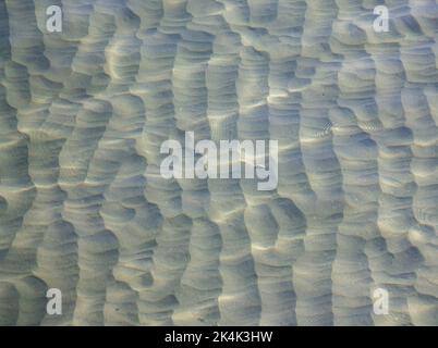 Fondale sabbioso o pavimento marino visto attraverso acqua di mare limpida con luce solare riflessa sulla superficie del mare. Foto Stock