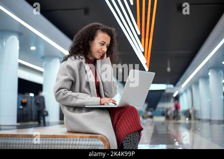 il blogger femminile utilizza un computer portatile mentre si siede su una panca in metropolitana. Foto Stock