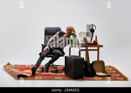 Uomo elegante, musicista rock seduto a casa e ascoltando musica. Stile retrò vintage. Musica, studio, emozioni tifosi, concetto di gioventù Foto Stock