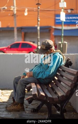 buon vecchio uomo, seduto in attesa, seduto sui gradini mentre si beve una cola, si possono vedere le colonne di una casa rossa Foto Stock