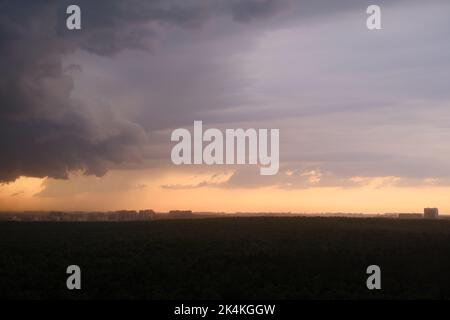 Cielo tempestoso al tramonto con nuvole di pioggia scure. Pioggia su una foresta estiva con alberi verdi Foto Stock