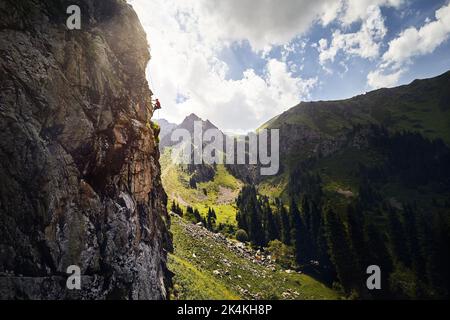 Adatta un atleta forte nella silhouette rock climbing sulla parete verticale alta sulle montagne Tyan Shan in Kazakistan Foto Stock