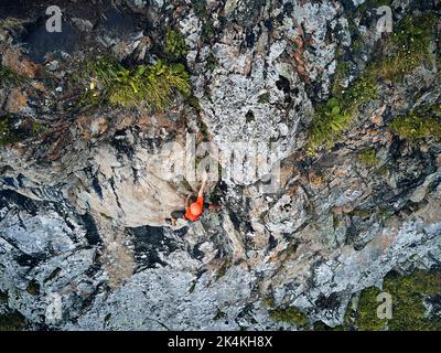 Fit forte atleta uomo in camicia rossa roccia arrampicata sulla parete verticale alta sulle montagne Tyan Shan in Kazakhstan. Vista dall'alto dall'alto dell'antenna a scatto con droni Foto Stock