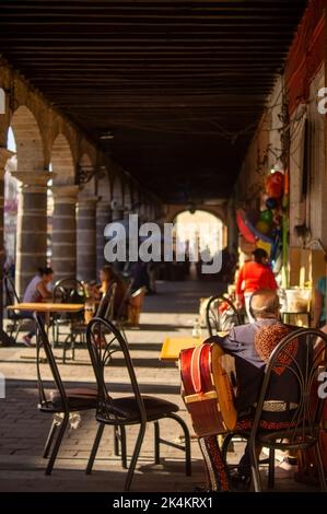 buon vecchio uomo, seduto in attesa, seduto sui gradini mentre si beve una cola, si possono vedere le colonne di una casa rossa Foto Stock