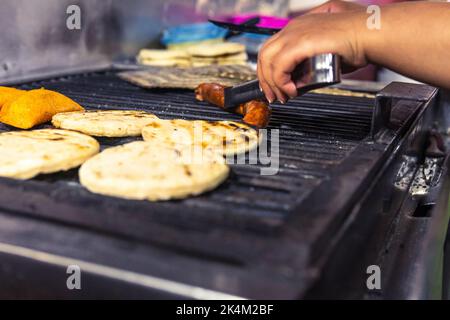 Primo piano selettivo delle mani che preparano il chorizo e gli arepi. Cucina colombiana tradizionale Foto Stock