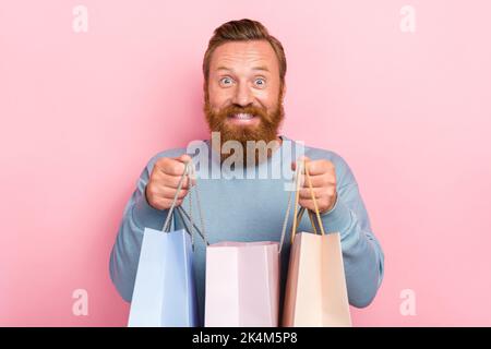 Ritratto di ecstatic impresso uomo zenzero barba vestita maglione blu soddisfatto tenendo borse della spesa isolato su sfondo di colore rosa Foto Stock