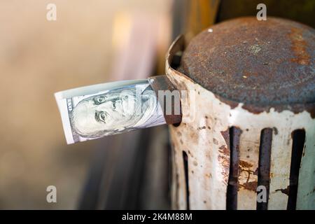 Un disegno di legge di cento dollari rotolato in un tubo sporge dal tubo di scarico di un trattore primo piano su uno sfondo sfocato. Tangenti e arresto del lavoro dovuto Foto Stock