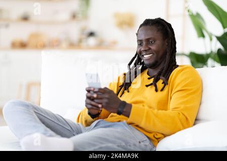 App Nizza. Sorridente afro-americano che si rilassa in sedia con smartphone Foto Stock