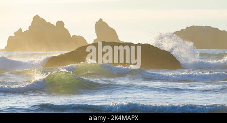 Mare retroilluminato di onde e formazioni rocciose nell'Oceano Pacifico con il picco del mare in forma ripetitiva di rocce Foto Stock