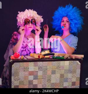 Le donne felici in divertenti parrucche danno una performance musicale su uno sfondo nero studio. Donne sorridenti che mostrano uno spettacolo divertente su uno sfondo scuro Foto Stock