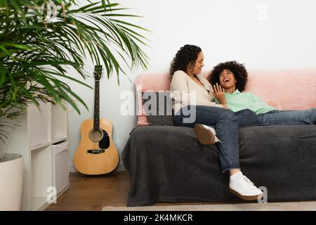 ragazza afroamericana eccitata che guarda la madre mentre riposa sul divano, immagine di riserva Foto Stock