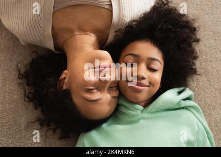 vista dall'alto di felice ragazza afro-americana sdraiata su tappeto con allegra madre, immagine stock Foto Stock