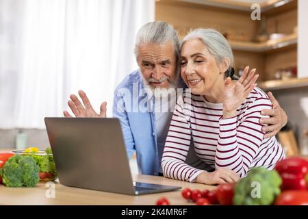 Allegri sposi anziani che fanno videochiamata con il laptop in cucina interno Foto Stock