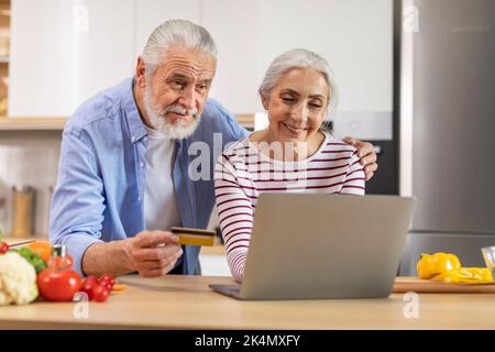 Senior Couple ordinare alimentari online con laptop e carta di credito in cucina Foto Stock