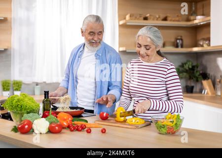Ritratto di sposi anziani allegri che preparano il pranzo in cucina insieme Foto Stock