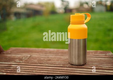 Thermos tazza con bevanda calda sullo sfondo. Il vapore proviene dalla tazza. Un theroms di vuoto di colore giallo sta su un ceppo dell'albero nel selvaggio. Foto Stock