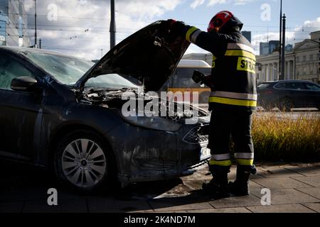 I membri del reparto antincendio sono visti mettere fuori un fuoco da un motore di automobile di Ford sulla piazza della banca (Plac Bankowy) a Varsavia, Polonia il 03 ottobre 2022. Foto Stock