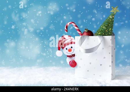 Pupazzo di neve di Natale con borsa della spesa sulla neve e regalo di Natale. Banner sconti invernali. Regali di consegna. Regalo Snowman Foto Stock