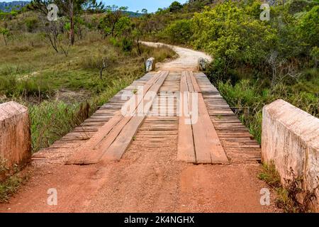 Strada sterrata con rustico e primitivo ponte in legno tra le colline e la vegetazione della riserva ambientale Biribiri di Diamantina Foto Stock