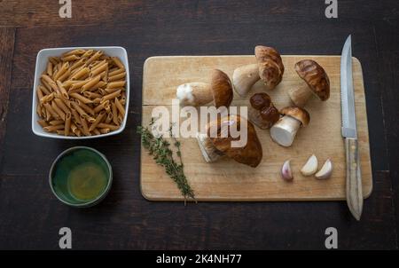 Vista dall'alto degli ingredienti per il piatto di funghi di pasta. Funghi porcini al boleto freschi, pasta, aglio, rosmarino e olio d'oliva sulla tavola Foto Stock