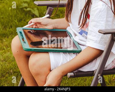 La ragazza fa le esercitazioni sul tablet in giardino Foto Stock