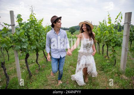 Giovane coppia corre romanticamente a piedi nudi attraverso il vigneto guardando gli occhi l'uno negli occhi dell'altro. Foto Stock