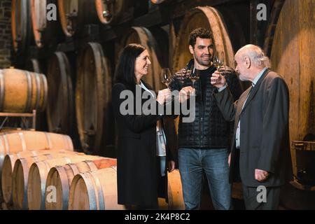 Ospiti della cantina, una donna e due uomini che degustano un vino bianco prodotto e invecchiato secondo antiche tradizioni in botti di rovere Foto Stock