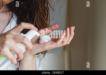 Donna che usa una mousse per lo styling dei capelli. Capelli ricci naturali, ondulati, primo piano Foto Stock