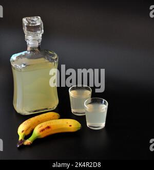 Liquore fatto in casa a base di banana, alcol forte e un paio di frutta matura su sfondo nero. Primo piano. Foto Stock