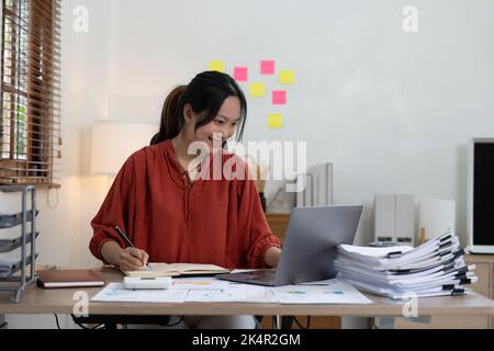 donna d'affari o contabile che prende nota e lavora alla calcolatrice e. computer portatile per calcolare i dati aziendali durante la registrazione a blocco note Foto Stock