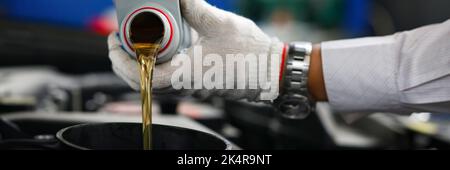Il meccanico automatico nei guanti versa l'olio motore nel motore Foto Stock