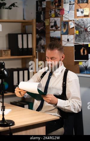 Agente FBI che analizza i risultati di studio esperto mentre ha lavorato al piano di ufficio, detective con clipboard Foto Stock