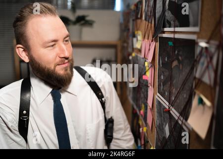 Ritratto di un detective professionista che guarda la scheda delle prove con foto e scene del caso in ufficio Foto Stock