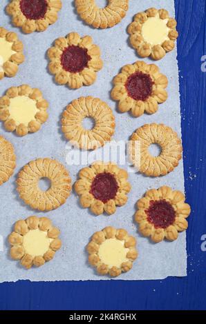 Diversi tipi di biscotti frollini dolci su carta situati su un tavolo di legno blu, vista dall'alto Foto Stock