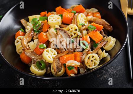 Rotelle pasta senza glutine con funghi e zucca su fondo scuro. Vegetariano, cibo vegano. Cucina italiana. Foto Stock